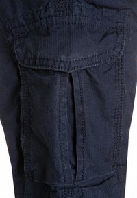 Námořnické cargo kalhoty z texturované tkaniny, které mají náprsní kapsy a kontrastní švy. Viditelné sklady zvyšují pohyblivost.