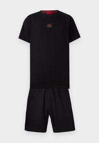 T-shirt noir à manches courtes avec un patch logo rouge sur la poitrine, associé à un short noir assorti sur fond blanc uni.