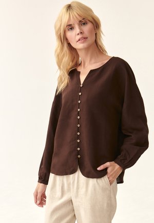 Bruine blouse met lange mouwen, V-hals en knoopsluiting aan de voorkant. Zachte textuur, losse pasvorm en afgeronde zoom. Combinatie met lichtgekleurde broek.