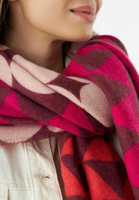 Écharpe colorée en tissu doux, présentant un motif géométrique de teintes rose, bordeaux et rouge, avec des bords effilochés et une variation de texture.