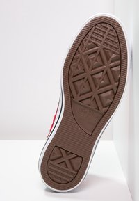 Suela de zapatilla de lona roja con un neumático de goma marrón texturizado que presenta un patrón de diamante y la marca "Converse All Star". Detalles blancos a lo largo del borde.