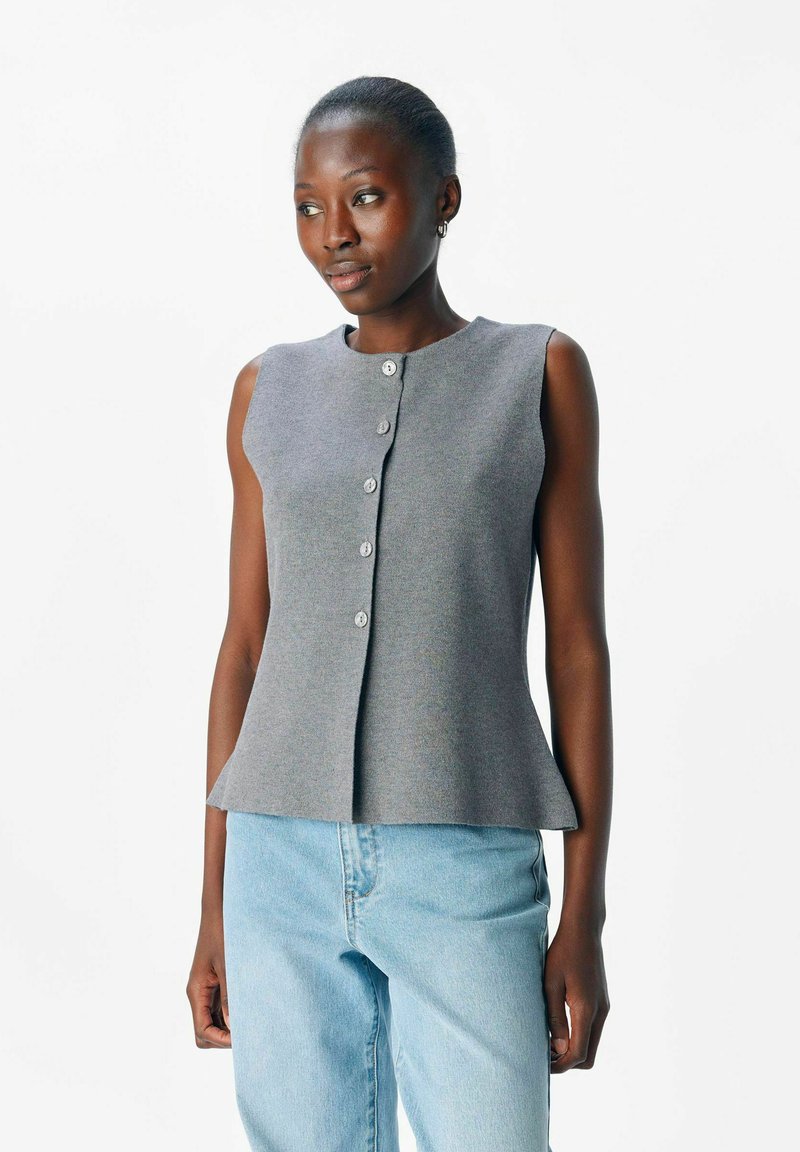 Graues ärmelloses Oberteil mit Rundhalsausschnitt, mit Knopfverschluss, Peplum-Saum und glatter Textur. Kombiniert mit hellblauen Jeans.