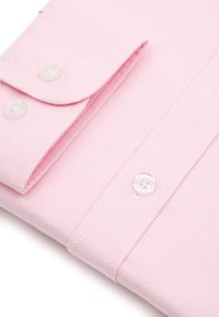 Rękaw koszuli z jasnoróżowej bawełny z białymi guzikami, starannie złożony, ukazujący teksturę tkaniny i szczegółowe przeszycia.