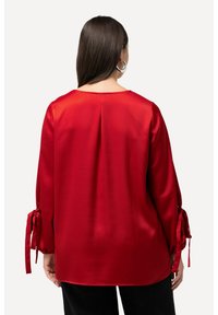 Blusa di raso rosso con maniche lunghe, presenta legature ai polsini, scollo a barca e un piega sul retro per aggiungere texture.