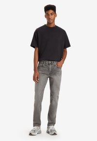 Black cotton t-shirt with a crew neckline paired with light grey denim jeans. Model wears grey sneakers. Simple design, relaxed fit.