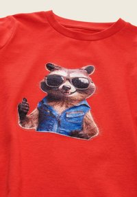 Rotes Baumwoll-T-Shirt mit einem Waschbären-Graphic, der eine Sonnenbrille und eine blaue Weste trägt und einen Daumen hoch zeigt.