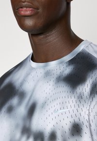 Nike athletic shirt in light gray with darker gray abstract patterns, featuring small perforations for breathability and a soft, smooth texture.