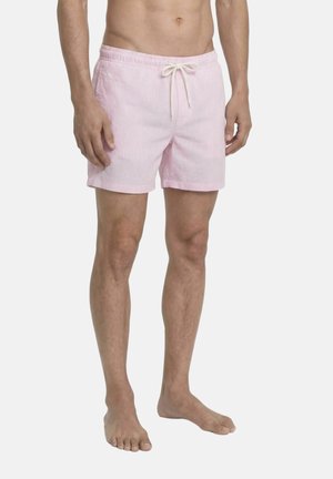Modèle masculin portant un short de bain rayé rose et blanc avec cordon de serrage, debout pieds nus sur un fond uni.