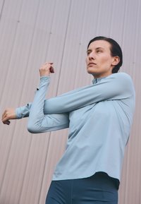 Light blue long-sleeve athletic top with a high neck and slim fit, featuring a smooth texture and subtle seam details.