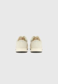 Baskets beige clair avec une tige en daim, des détails en mesh contrastants et une semelle en caoutchouc noir texturé. Logo ASICS à l'arrière.