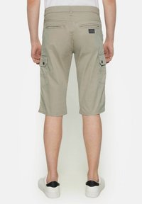 Pantalones cortos cargo beige con corte recto, dos bolsillos laterales y detalles de costura sutiles. Llevados con zapatillas blancas, vista desde atrás.