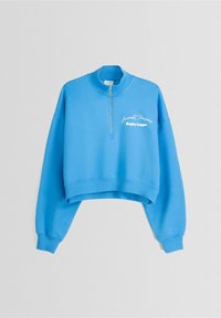 Sudadera azul recortada con cuello alto, cierre de media cremallera y puños acanalados. Presenta texto bordado en blanco en el frente.