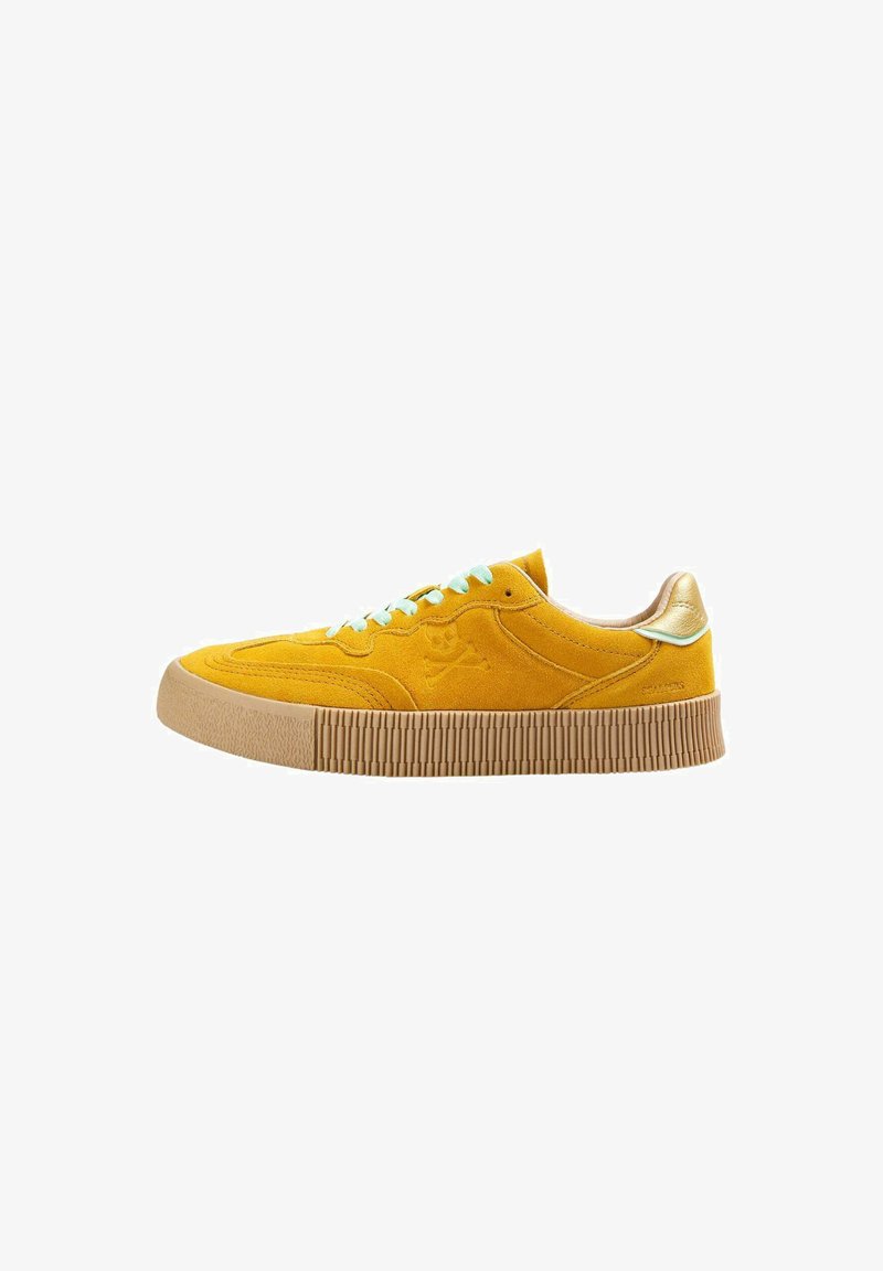 Baskets en daim jaune avec une semelle en caoutchouc texturé, lacets bleu clair et un accent en métal doré au talon. Présente un logo de skull et os croisés.