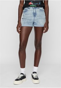 Šviesiai mėlyni džinsiniai šortai su suplėšytu kraštu, aukštu liemeniu ir sukamu kojų kraštu. Pora su juodais sportbačiais ir baltais kulkšnies kojinėmis.