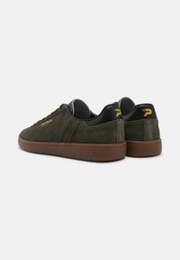 Sneakers in suede verde scuro con suole in gomma marrone. Presentano accenti neri e branding dorato sul tallone e sul lato. Design classico a bassa altezza.