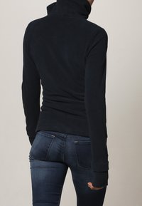 Suéter de cuello alto de manga larga en azul marino, hecho de material suave; diseño ajustado con puños acanalados y un cuello alto; combinado con jeans de mezclilla oscura.