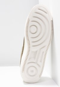 Semelle en caoutchouc blanche d'une basket Nike avec des motifs de bande de roulement circulaires et linéaires, photographiée sur fond blanc.