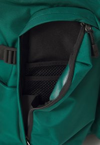 Interior de mochila verde-água com um bolso de rede preto. Apresenta um fecho e compartimentos adicionais, mostrando um tecido resistente e um design funcional.