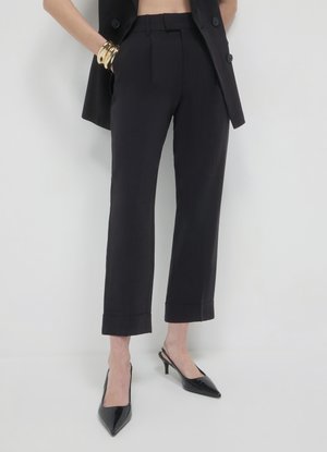 Pantaloni neri su misura con gamba dritta, orlo corto e pieghe frontali, abbinati a décolleté nere slingback con punta affilata.