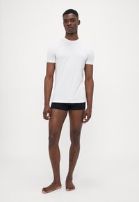 Weißes kurzärmliges T-Shirt, taillierte Passform, getragen mit schwarzen Unterwäsche, minimale Nähte, glatte Textur und keine sichtbaren Muster oder Logos.