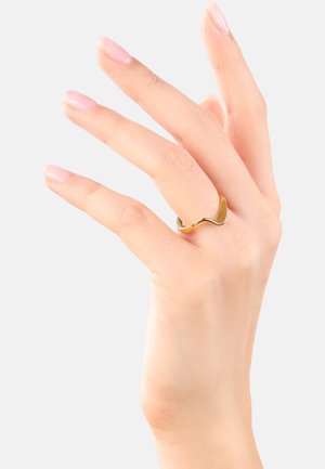Anillo de metal dorado con un diseño ondulado, textura suave y acabado pulido, exhibido en una mano con uñas de color rosa claro.