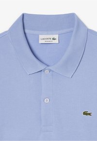 Polo shirt azzurro chiaro con colletto classico, due bottoni e logo di coccodrillo verde ricamato sul lato sinistro del petto. Design a vestibilità regolare.