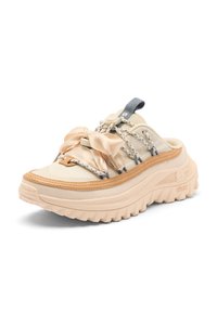 Beige slip-on sneaker with thick sole, rope laces, and decorative satin bow on top, photographed on white background.
