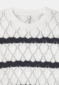 White knit sweater with diamond-shaped openwork pattern and two horizontal black stripes across the chest and waist area.