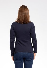 Maglietta a maniche lunghe navy in morbido tessuto, con scollatura tonda e taglio aderente, abbinata a jeans blu scuro.