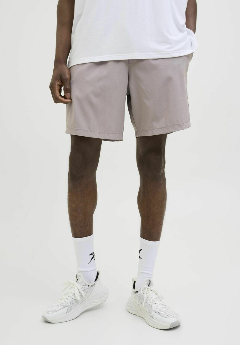 Pantalones cortos beige claro hechos de tejido sintético, con bolsillos laterales y un ajuste relajado. Combinados con zapatillas blancas y calcetines hasta el tobillo.