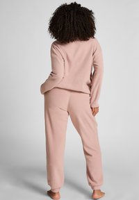 Jasnoróżowy, przytulny dres, wykonany z miękkiego polaru o luźnym kroju. Posiada ściągacze przy rękawach i nogawkach dla większego komfortu. Brak widocznych wzorów lub dodatków.