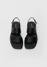 Mustad mustad nahast sandaalid, millel on kaks laia rihma, neljnurkne varvas ja slingback disain. Omab rihmal reljeefset logo ja madalat tallat.