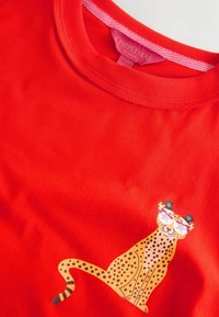 Tricou roșu cu mânecă scurtă și decolteu rotund, prezentând un grafic cu o ghepardă purtând ochelari, împodobită cu accente decorative.