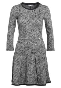 Robe en chevron noir et blanc à manches longues, encolure ronde, jupe plissée, avec un bord noir le long de l'encolure et de l'ourlet.