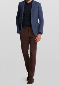 Marinblå tweedblazer över en mörk polo, i kombination med bruna chinos och bruna mockaanklarstövlar, med en figurnära silhuett och subtila texturer.