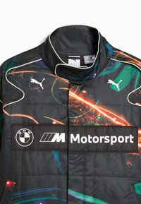 Svart racingjacka med livfulla färggrafik, hög krage och tydliga logotyper för BMW och Puma. Kviltad textur synlig.