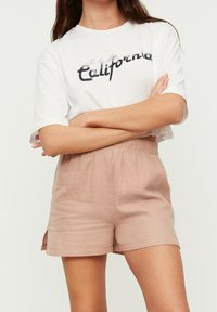 Maglietta corta bianca con la scritta "California" stampata in nero, abbinata a pantaloni corti elastici rosa chiaro con fessure laterali.