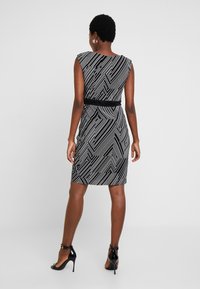 Šaty s geometrickým vzorem v černobílé barvě, s přiléhavým střihem, krátkými rukávy a černým pasem. Nosí se s černými lodičkami na vysokém podpatku.