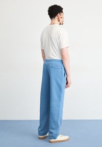 Gaiši zili sporta bikses brīvā piegriezuma, ar elastīgu jostasvietu un aizmugurējo kabatu, apvienotas ar neitrālu t-kreklu un baltām kedām.