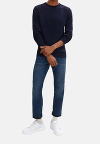 Granatowy sweter dzianinowy z długimi rękawami, sparowany z jasnoniebieskimi spodniami o prostym kroju i białymi sneakersami. Swobodny, wygodny strój.