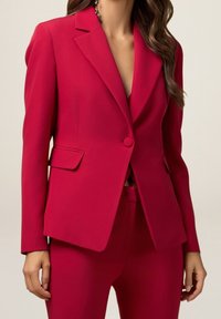 Blazer ajusté en rose vif. Dispose de revers en chevron, fermeture à un bouton, poches latérales et tissu lisse avec une silhouette cintrée.