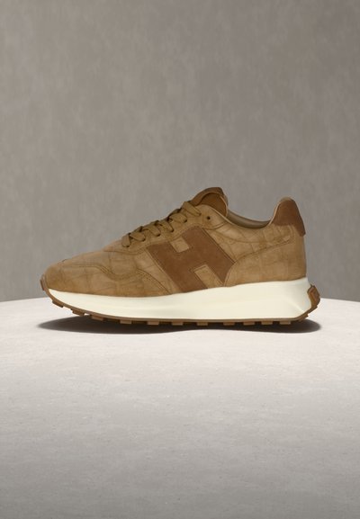 Baskets en daim marron avec motif texturé, lacets ton sur ton, col rembourré et semelle blanche amortissante sur une surface et un fond gris clair.