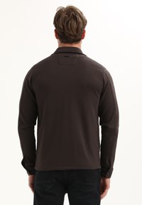 Polo a maniche lunghe marrone scuro con polsini con bottone, texture liscia e dettagli delle cuciture, con un piccolo etichetta sul retro vicino al colletto.