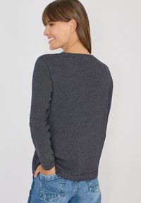 Maglietta a maniche lunghe a righe grigio scuro con colletto rotondo e tessuto testurizzato, abbinata a jeans in denim chiaro.