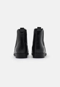 Botas de tobillo de cuero negro con paneles laterales elásticos, punta afilada y un tacón bajo apilado. Textura suave con un hardware mínimo.