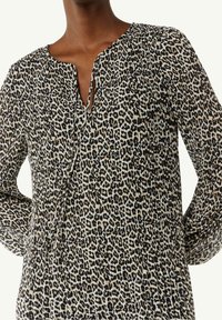 Blouse en imprimé léopard avec un décolleté en V plongeant, des manches longues et une texture plissée dans des tons de beige, noir et marron. Tissu doux.
