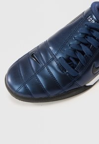 Tengerészkék bőr focicipő elegáns kialakítással, texturált felülettel, vízszintes varrással és fekete gumi talppal. Nike logó az oldalon.