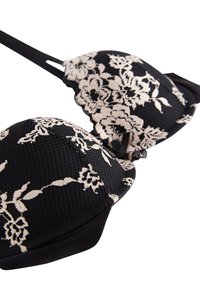 Reggiseno nero con coppe sagomate, caratterizzato da una sovrapposizione in pizzo floreale color crema. Ha spalline regolabili e una fascia liscia e testurizzata.