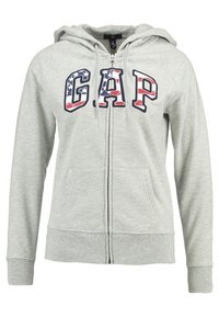 Sweat à capuche gris zippé en tissu doux. Il présente un grand logo "GAP" en rouge et bleu, des poches avant, et une capuche à cordon.