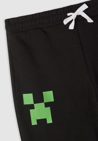 Pantaloni della tuta neri realizzati in un mix di cotone, con un design pixelato verde sulla gamba sinistra e una vita elastica con coulisse bianca.